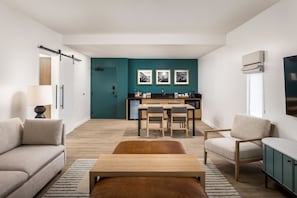 A modern living room with a sofa, a wooden coffee table, and a teal accent wall. - Guesthouse Hotel at La Valle (Rancho Santa Fe)