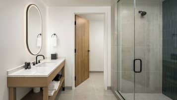Un baño moderno con tocador de madera, un espejo grande y cabina de ducha con paredes de vidrio.