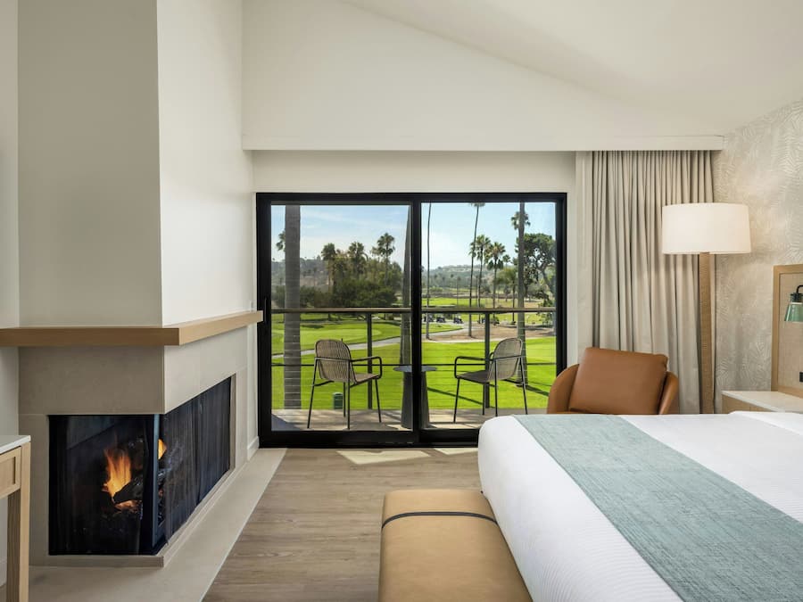 Una habitación de hotel con una cama grande, una chimenea, un televisor y un balcón con vista a un campo de golf.