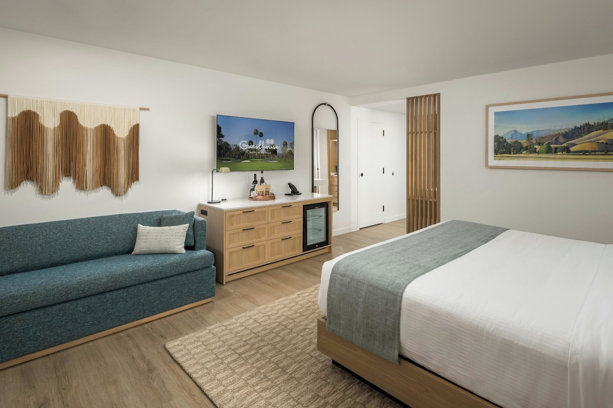 A bedroom with a bed, a sofa, a TV, a desk, and a painting.