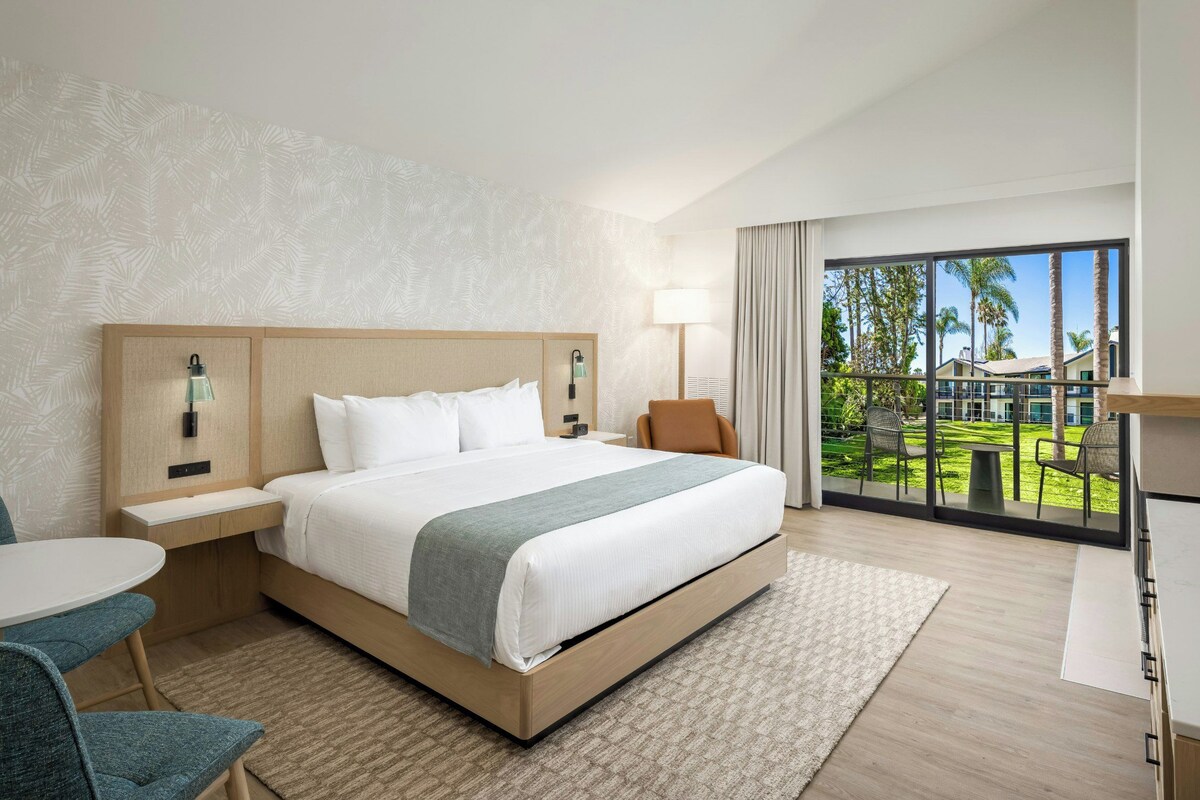 A hotel room with a large bed, a desk, a chair, and a view of the outdoors.