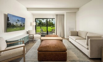 Een moderne hotelkamer met een groot raam met uitzicht op een golfbaan, een flatscreen-televisie aan de muur, een bank, een stoel en een klein tafeltje.