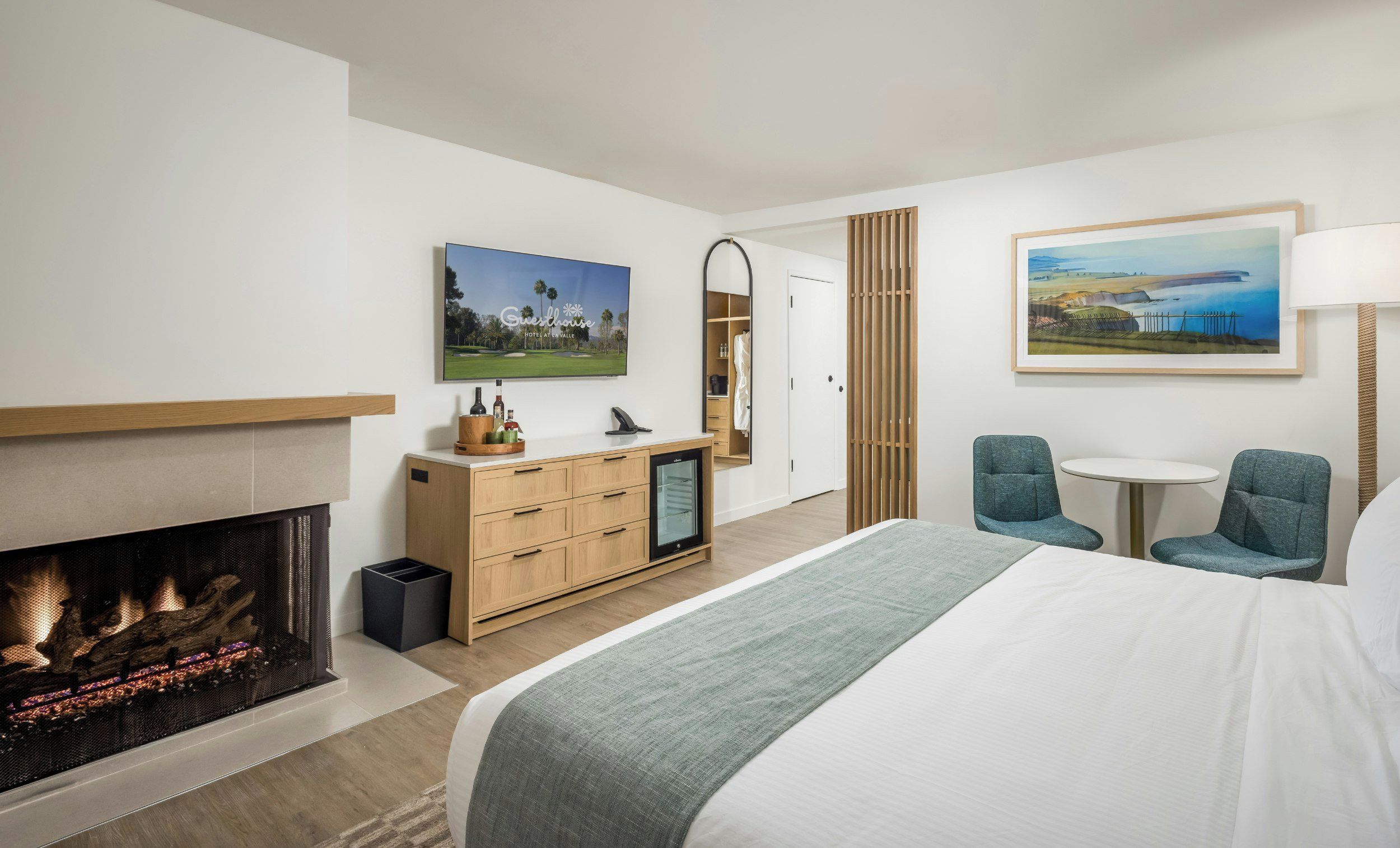 A modern hotel room with a fireplace, a bed, a desk with a computer, and two chairs.