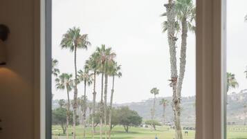 A room with a large window overlooking a golf course, a chair, and a table.