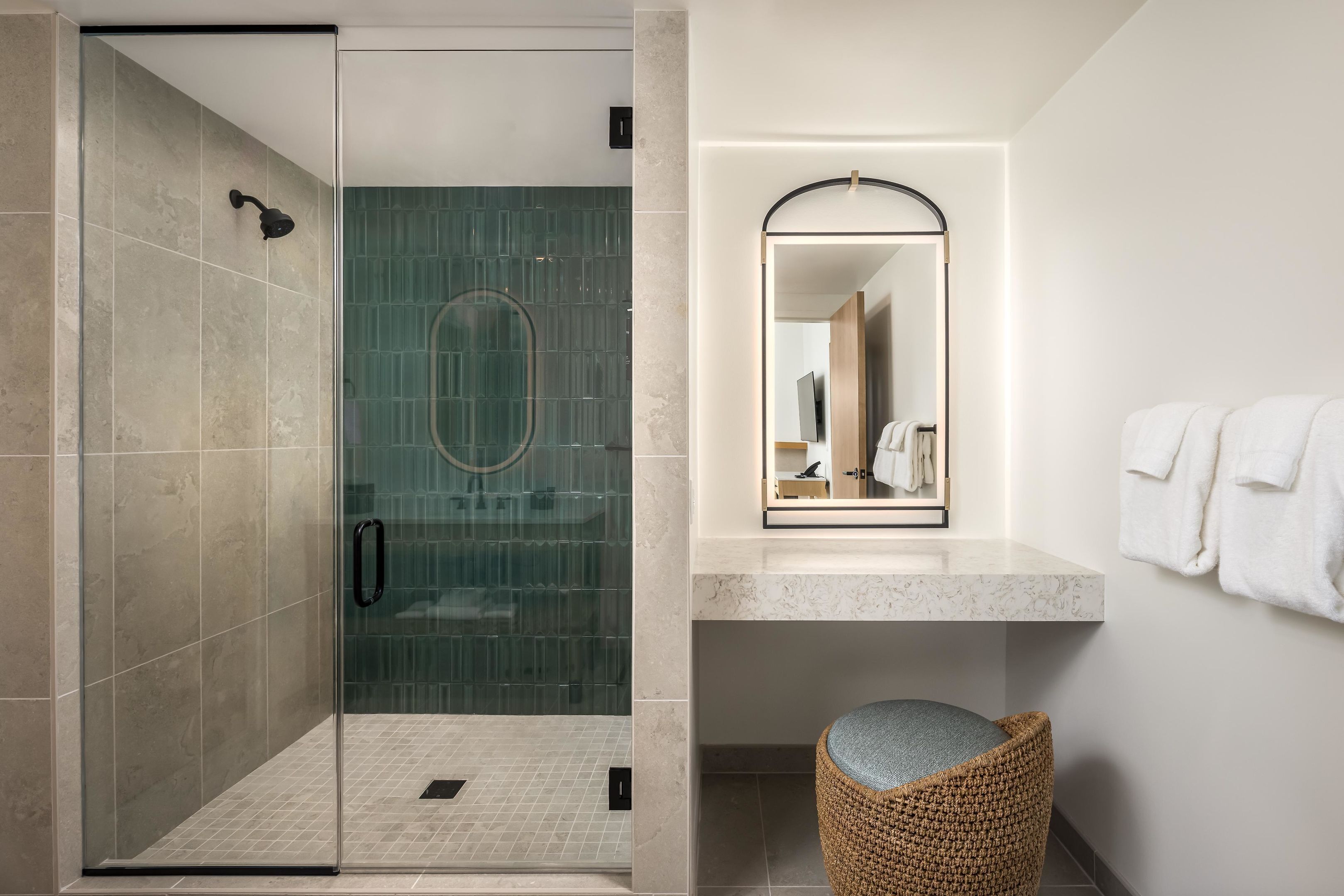 A modern bathroom with a glass-enclosed shower, a marble sink, and a woven stool.