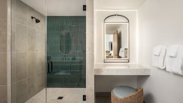 A modern bathroom with a glass-enclosed shower, a marble sink, and a woven stool.
