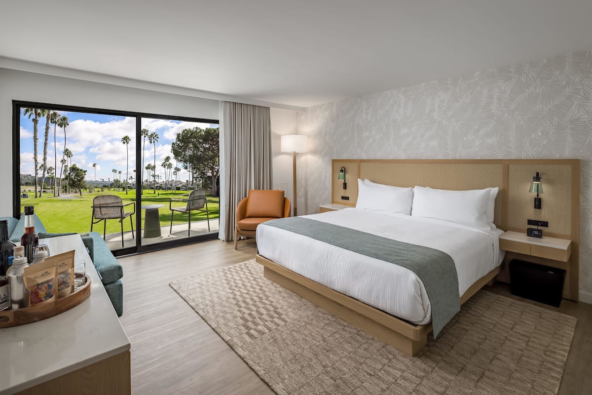 A hotel room with a large bed, a desk with a coffee maker, a chair, and a view of a golf course.