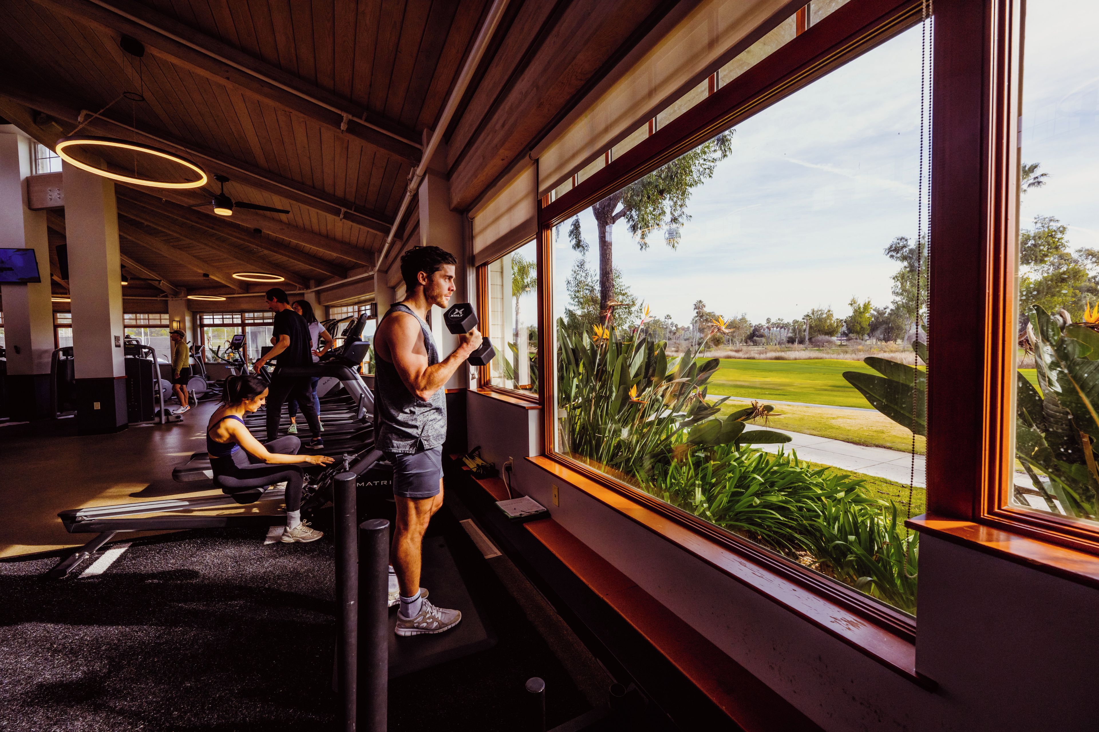 A gym with exercise equipment and large windows overlooking a golf course.