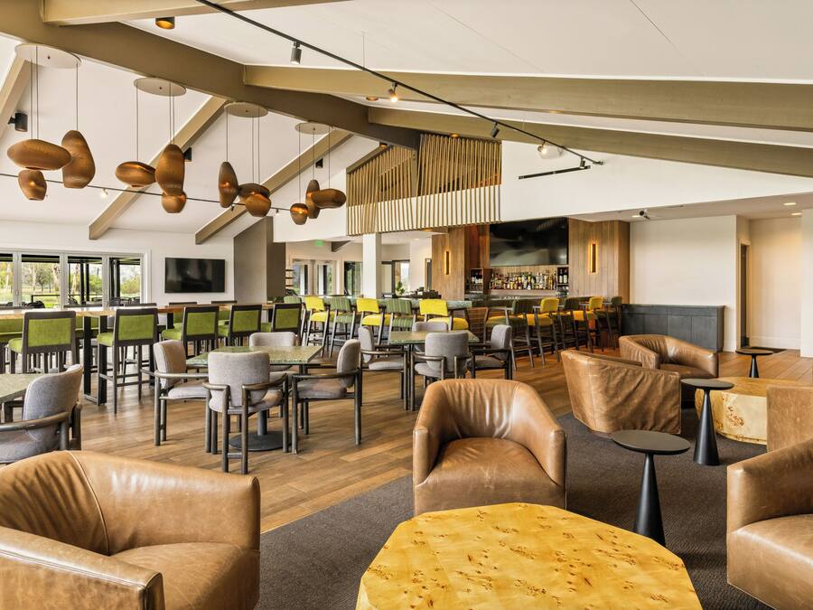 Een ruime binnenzone met diverse zithoekjes, waaronder leren fauteuils en tafels, plus een bar met verschillende soorten zitplaatsen.