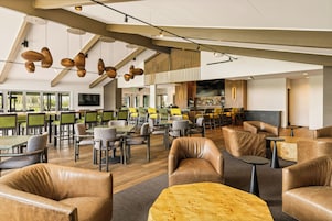 Een ruime binnenzone met diverse zithoekjes, waaronder leren fauteuils en tafels, plus een bar met verschillende soorten zitplaatsen.