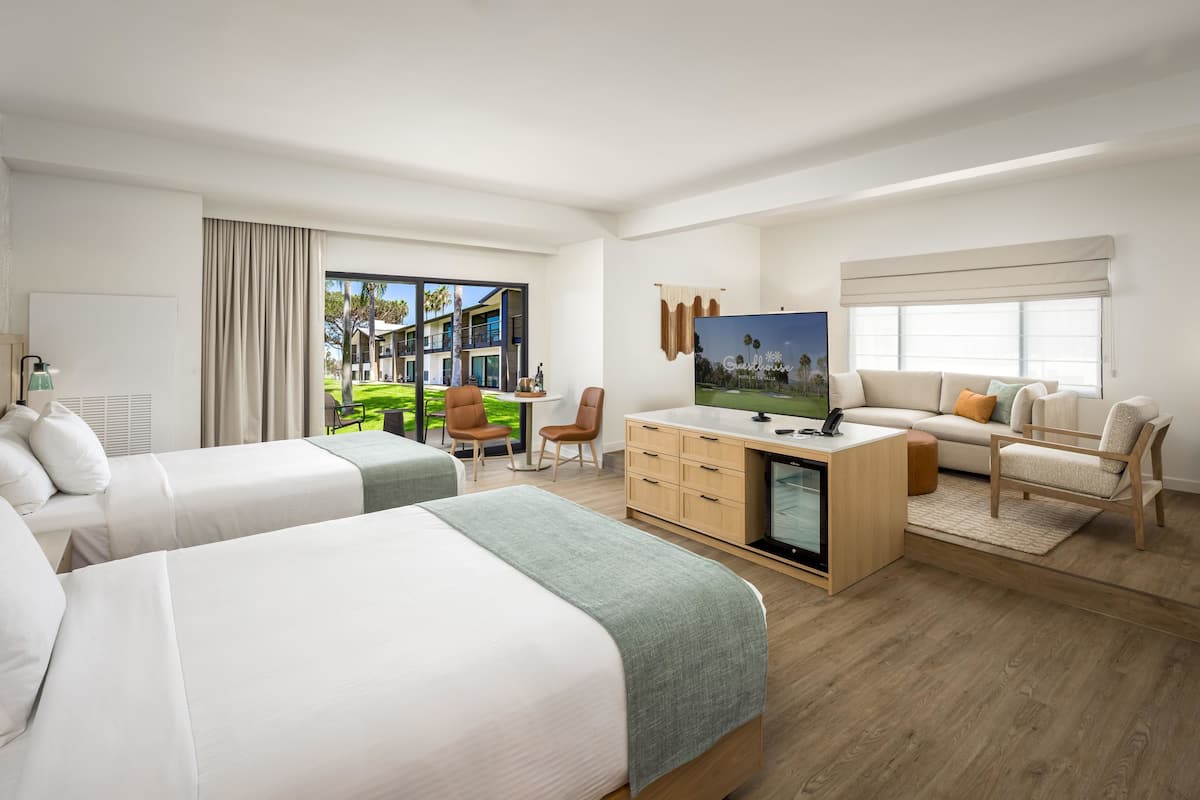 A hotel room with two beds, a desk, a television, and a view of the outdoors.
