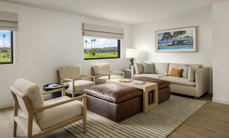 Een moderne woonkamer met een bank, twee fauteuils, een salontafel en uitzicht op een golfbaan door het raam.