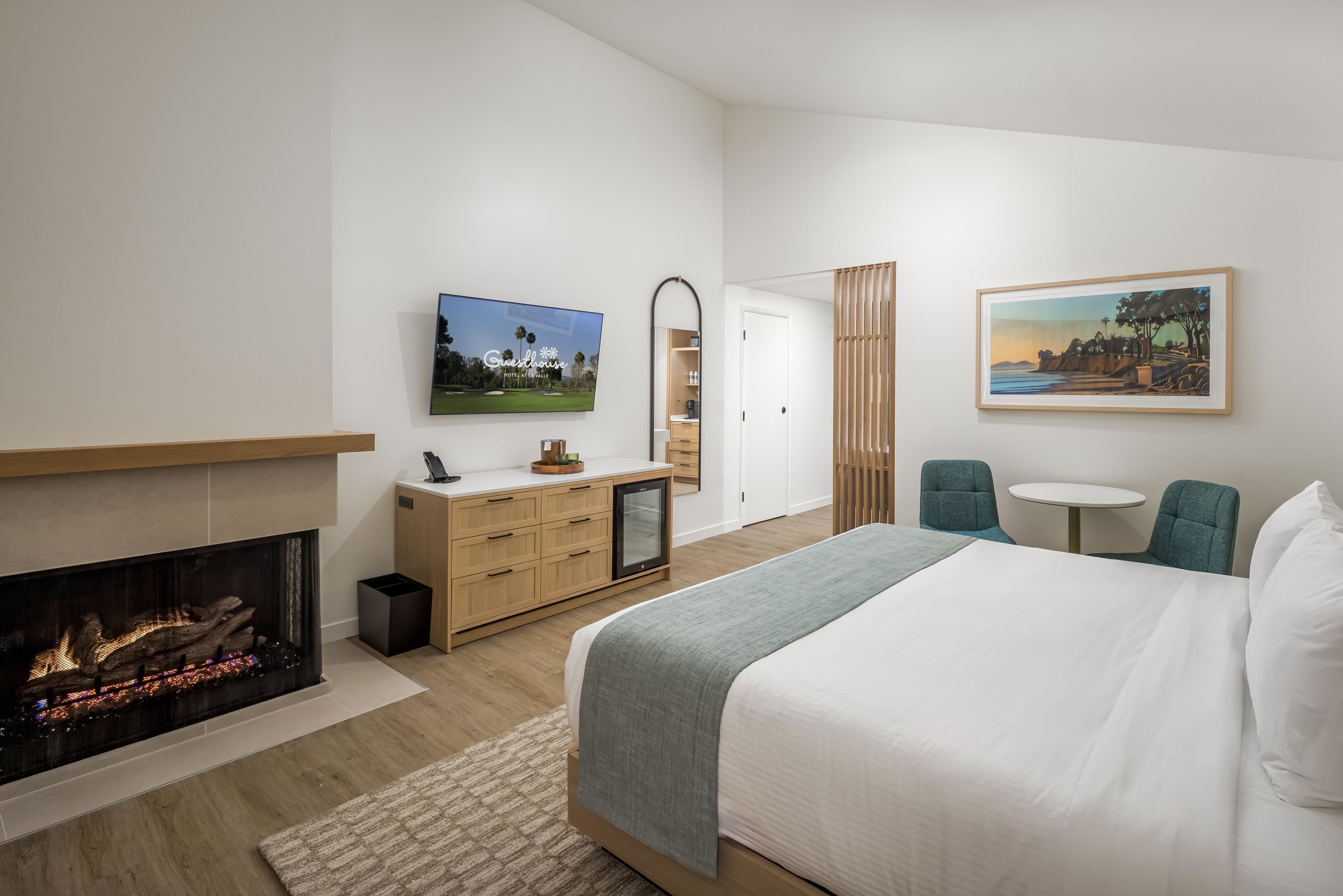 Una habitación de hotel moderna con chimenea, una cama, un escritorio con silla, una mesita y obras de arte en las paredes.