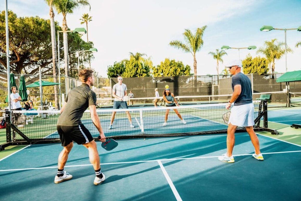 Cancha de tenis al aire libre con red, jugadores y espectadores.