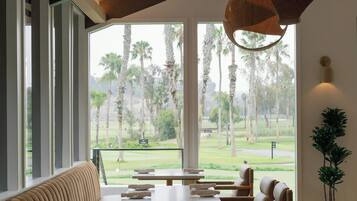 Un restaurante con una larga banqueta, mesas con platos y lámparas de madera colgantes.
