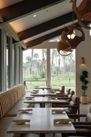 Een restaurant met een lange bankzitting, tafels met borden en hangende houten lampen.