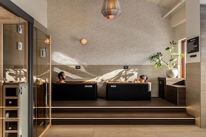 A modern reception area with glass doors, two black reception desks labeled 'COLDER,' a large potted plant, and a textured ceiling with a hanging light fixture. - Guesthouse Hotel at La Valle (Rancho Santa Fe)