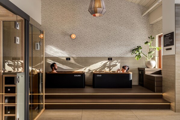 A modern reception area with glass doors, two black reception desks labeled 'COLDER,' a large potted plant, and a textured ceiling with a hanging light fixture. - Guesthouse Hotel at La Valle (Rancho Santa Fe)