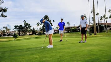 Golfers enjoy a round on the well-manicured course surrounded by palm trees and residential buildings.