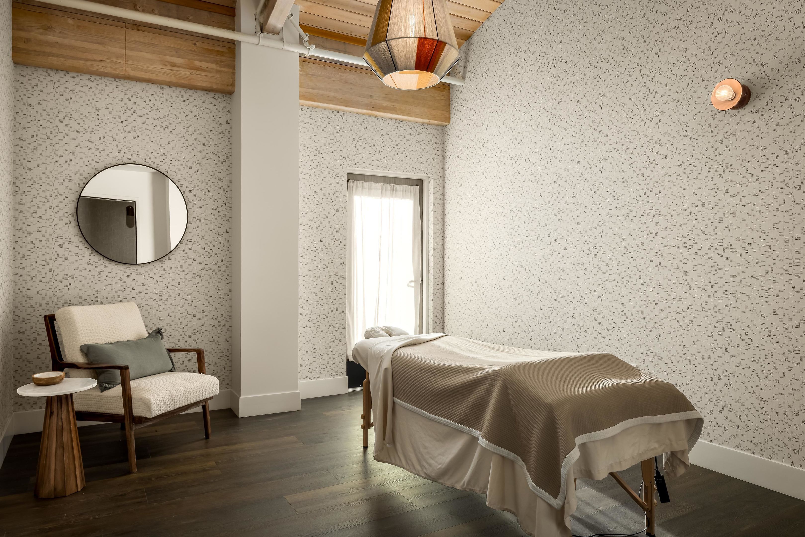 A room with a bed, a chair, a round mirror, and a small table.