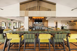 A spacious bar area with a long counter and multiple stools, a bar stocked with various bottles, and a television mounted on the wall.
