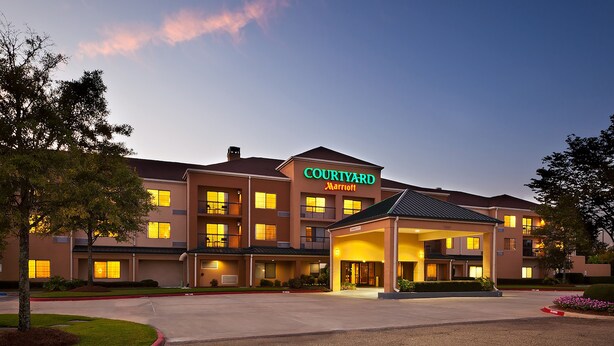 Ein Courtyard Marriott Hotel mit mehreren Etagen, einem überdachten Eingang und einem gepflegten Rasen.