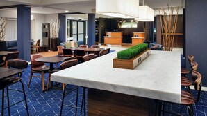 Eine Hotelhalle mit Marmor-Rezeption, einer Sitzecke mit Tischen und Stühlen sowie dekorativen Pflanzen.