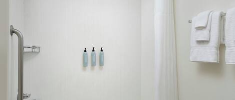 A bathroom with a white bathtub, a showerhead, a grab bar, and three bottles of shampoo on the wall.