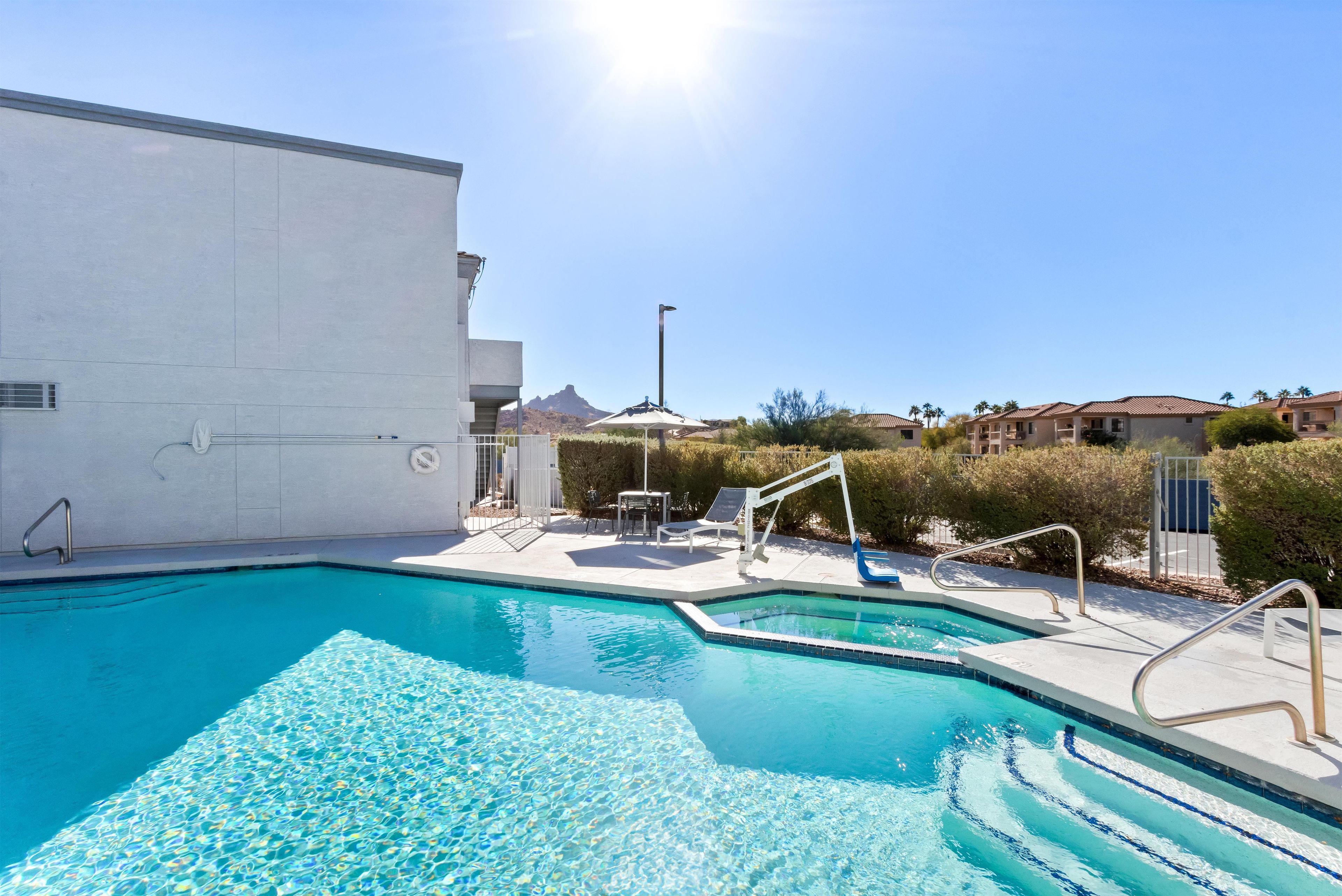A clear blue pool with steps leading into it, surrounded by a white building and a clear sky.