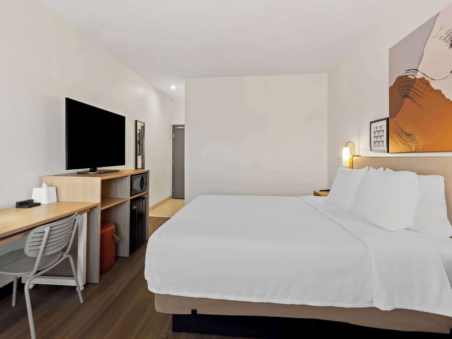 Habitación de hotel con cama, escritorio con silla, televisión y un cuadro en la pared.