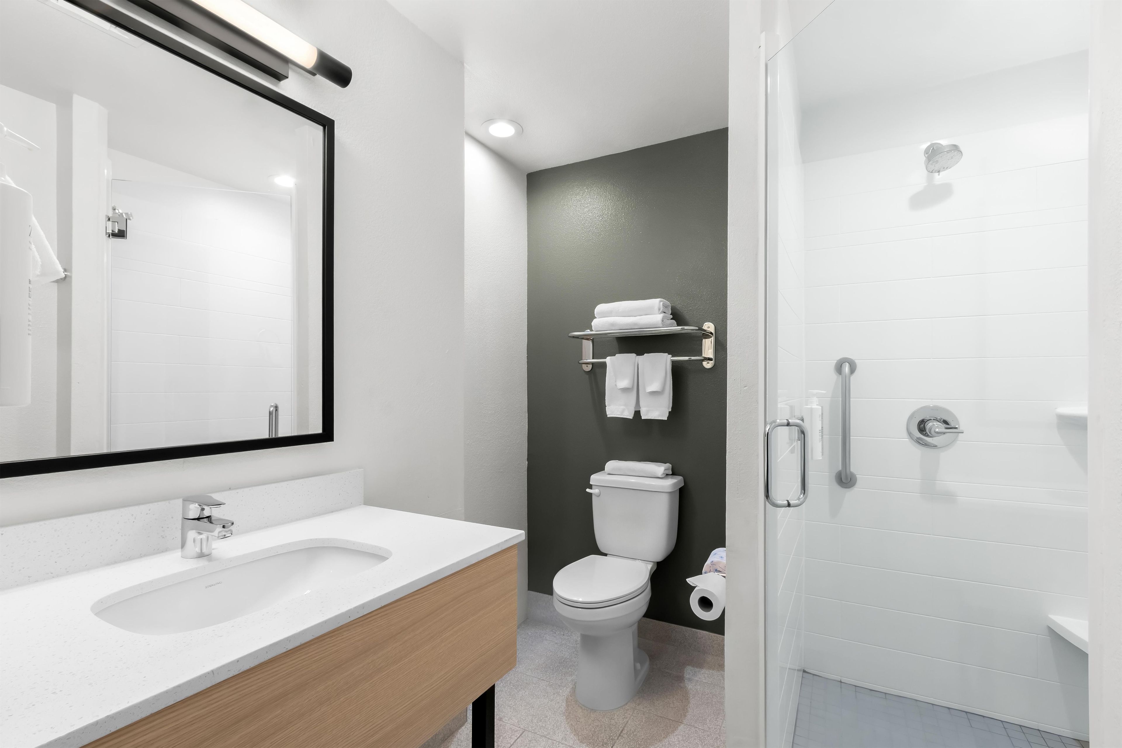 A modern bathroom with a white sink, a mirror, a toilet, and a shower area.