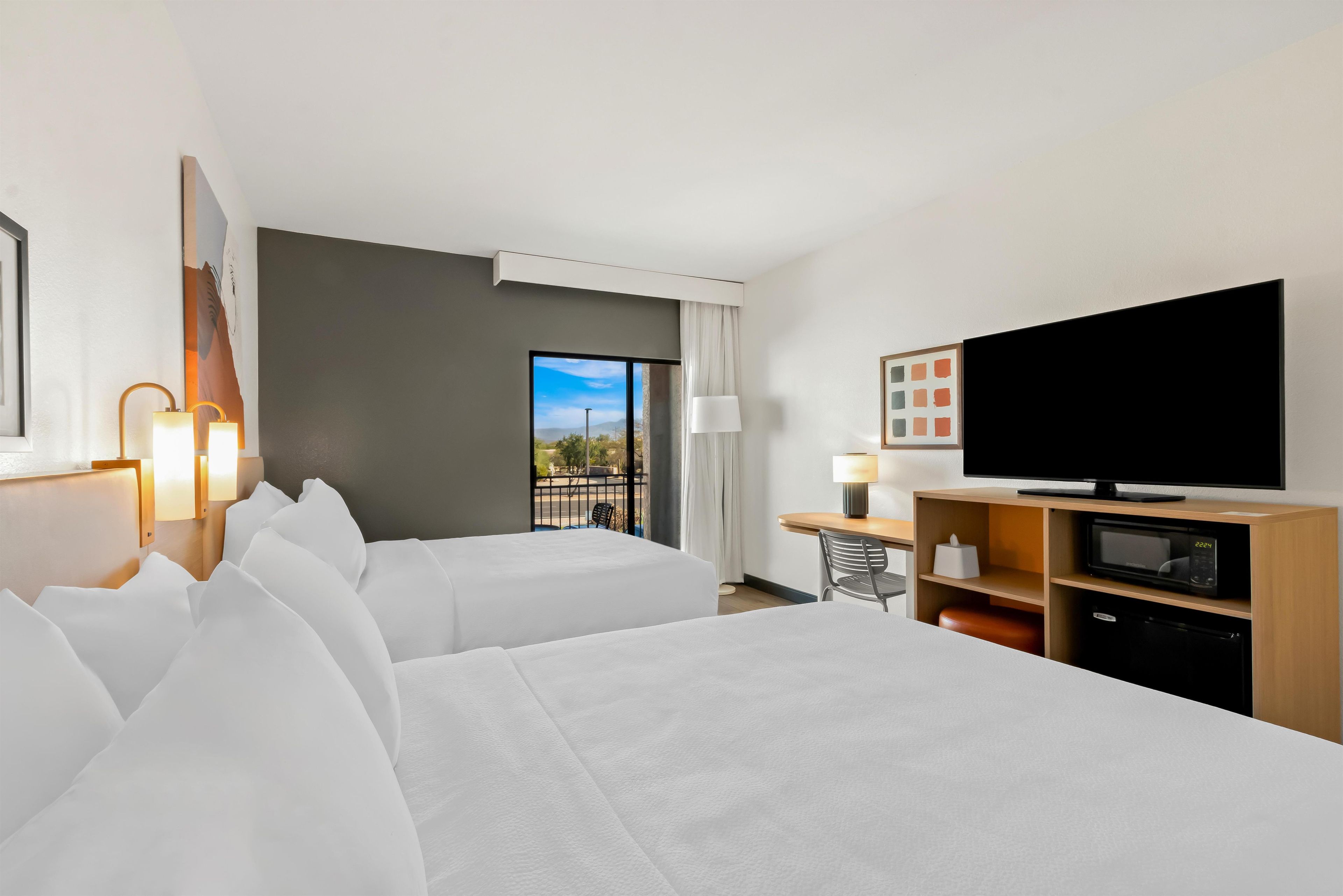 Habitació d'hotel amb dos llits, televisió, escriptori amb làmpada i vista a l'exterior.