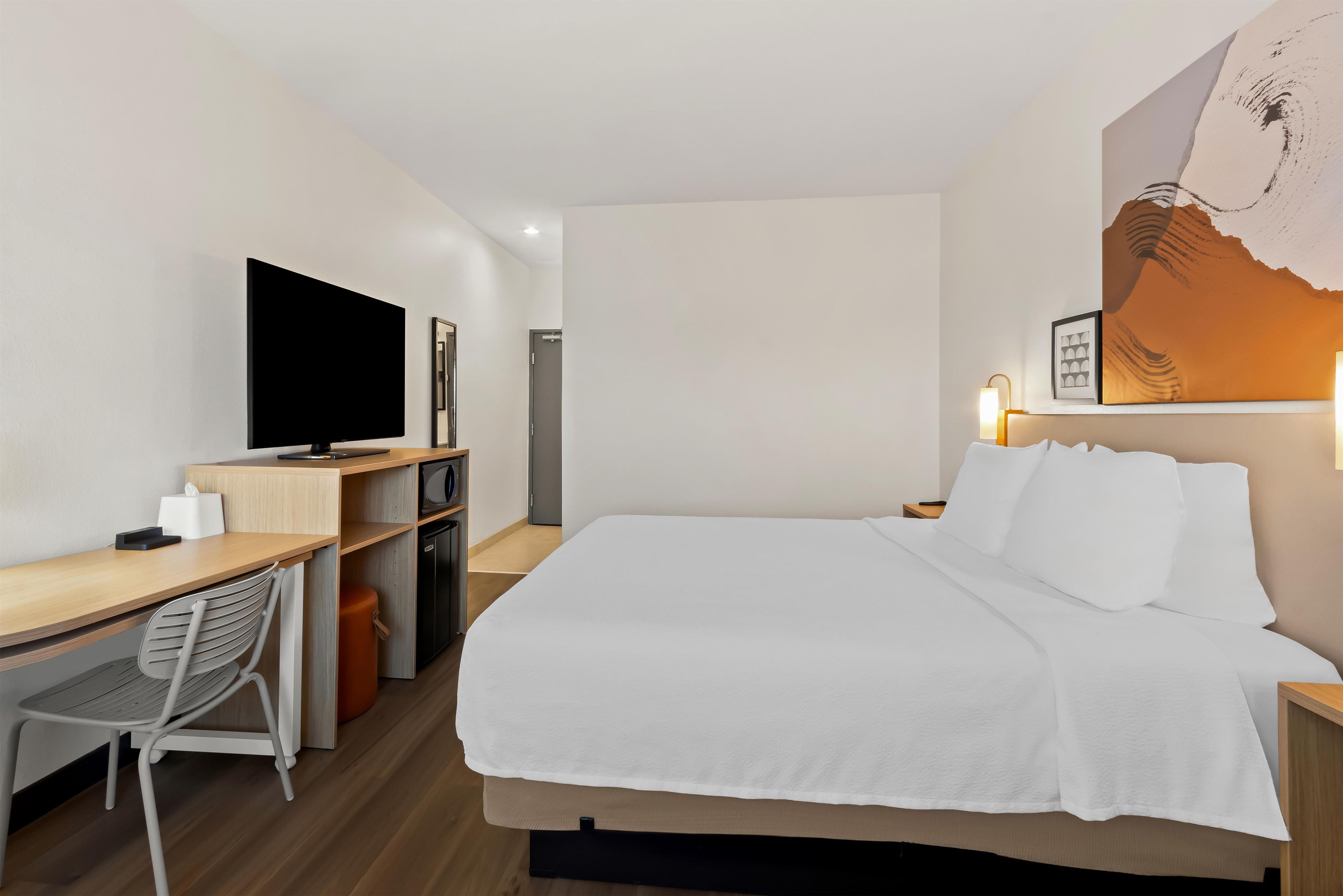 A hotel room with a bed, a desk, a television, and a chair.