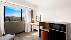 A modern hotel room with a large window, a desk with a lamp, a microwave, and a chair. - Spark by Hilton Fountain Hills Scottsdale (Fountain Hills)