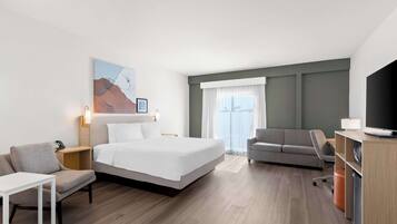 A hotel room with a bed, a sofa, a desk, a TV, and a painting on the wall.