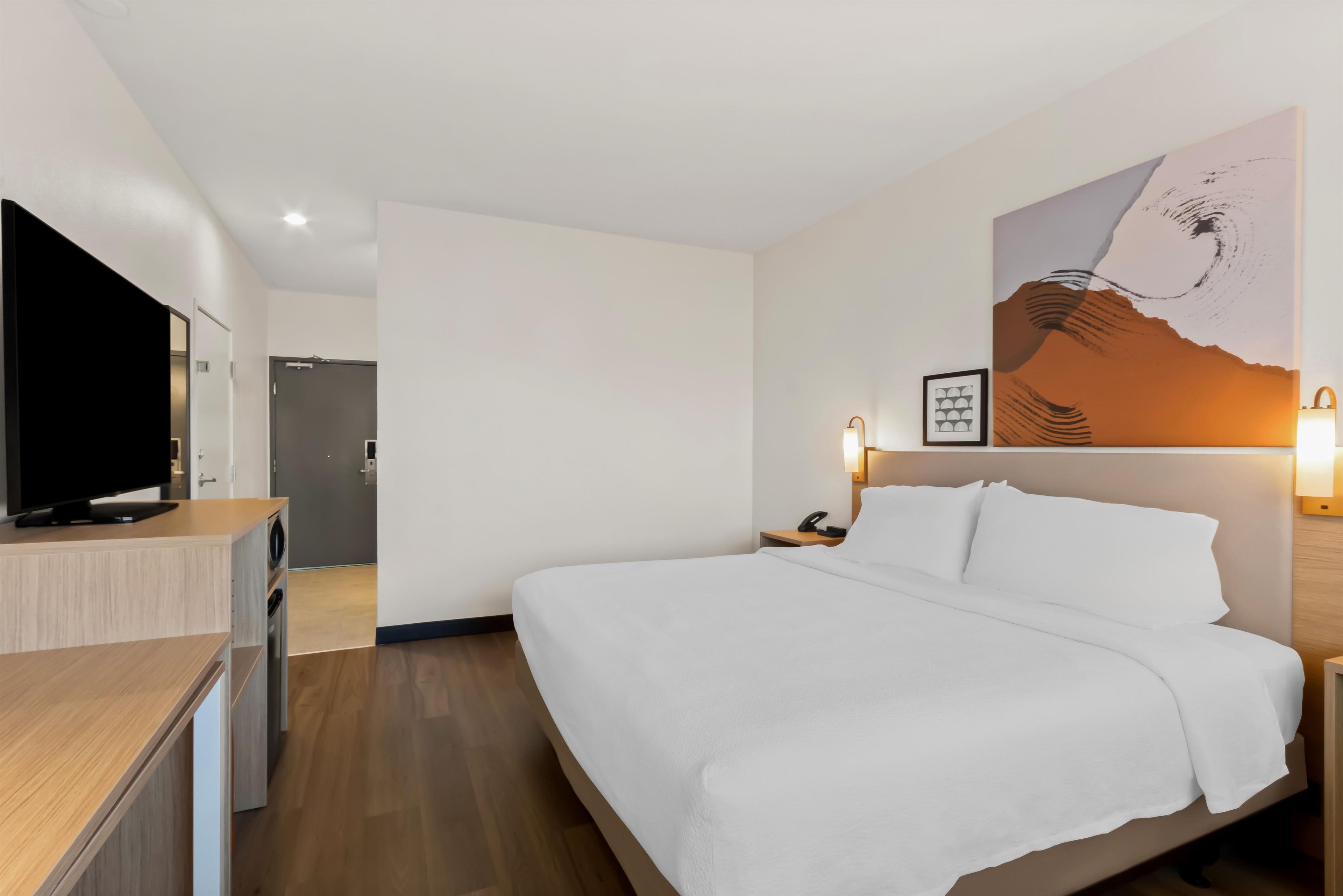 Una habitación de hotel con una cama, televisor, un cuadro y un escritorio.