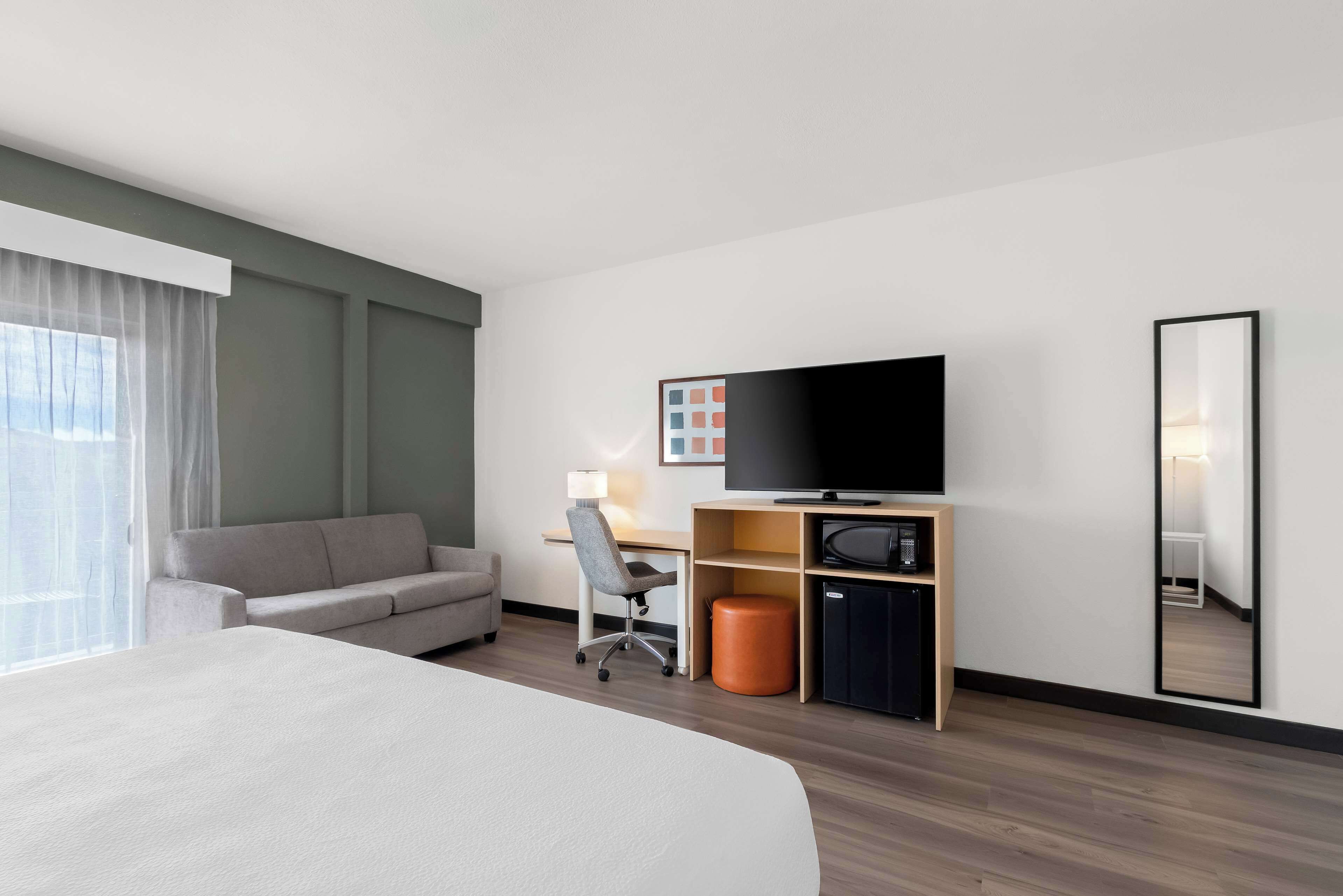 Een hotelkamer met een bed, een bank, een bureau met stoel, een televisie en een spiegel.