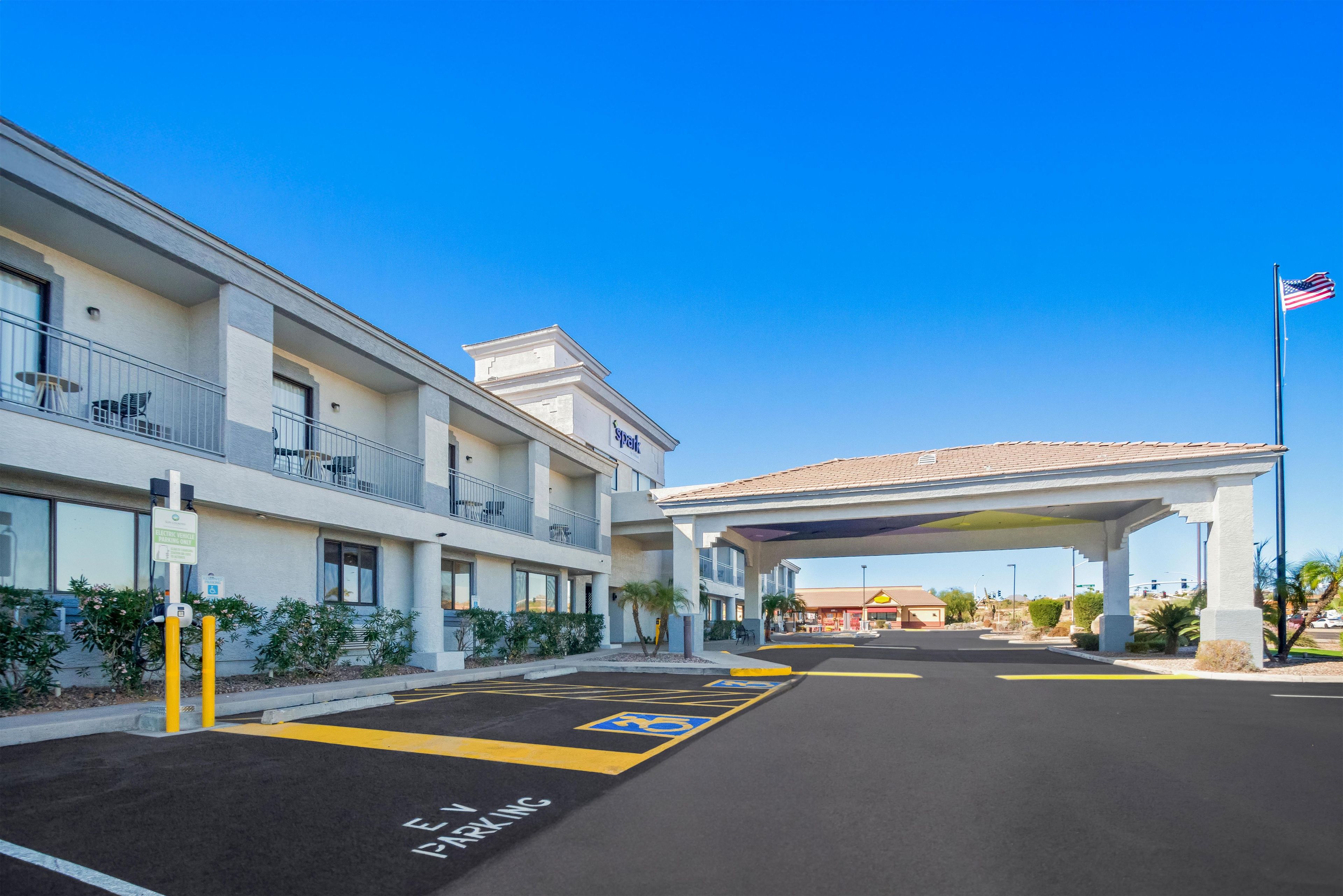 Un hotel con un estacionamiento señalizado para vehículos eléctricos, un corredor cubierto y un cielo azul despejado.
