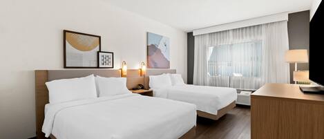 Una habitación de hotel con dos camas, un escritorio, una lámpara y obras de arte en la pared.