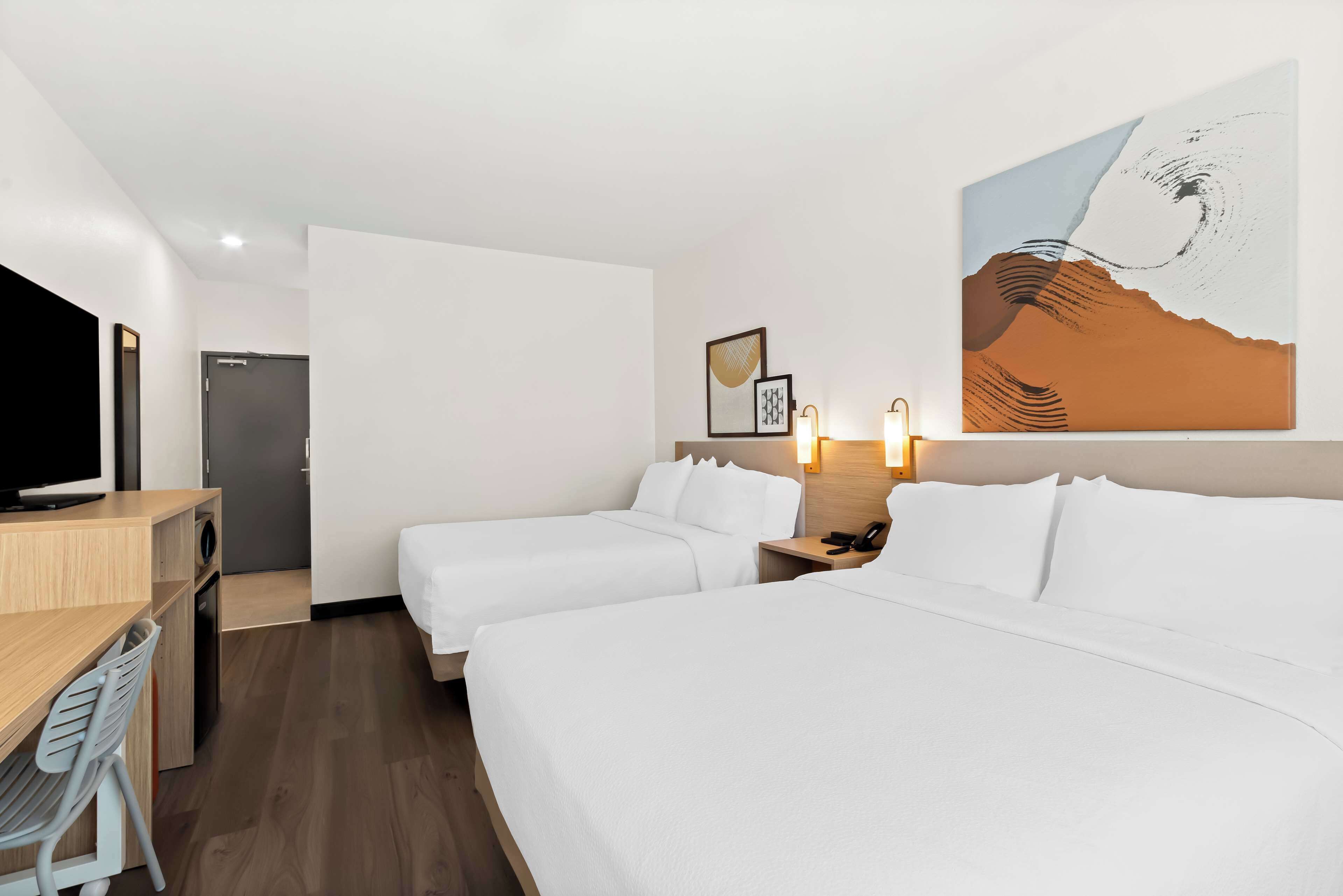 A hotel room with two beds, a desk with a chair, a television, and artwork on the wall.