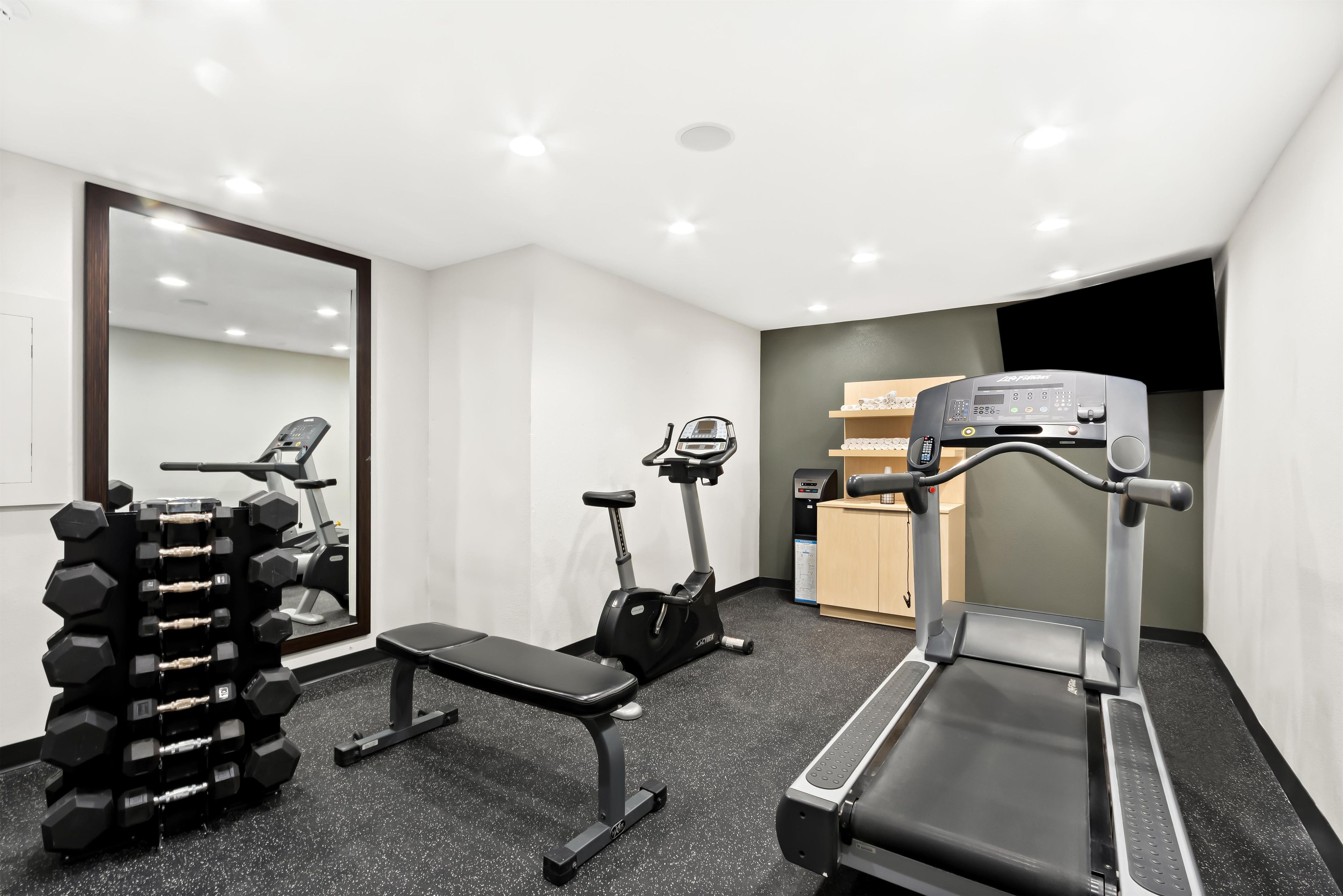 Un gimnasio con cinta de correr, elíptica y banco.