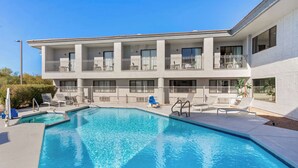 A pool area with a clear blue pool, lounge chairs, and a multi-story building with balconies. - Spark by Hilton Fountain Hills Scottsdale (Fountain Hills)