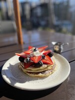 A dessert on a white plate with powdered sugar, topped with strawberries, blueberries, and blackberries.