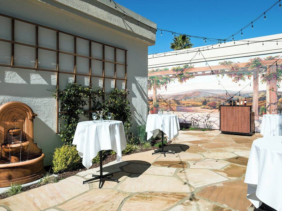 Un patio al aire libre con suelo de piedra, mesas blancas y una fuente.