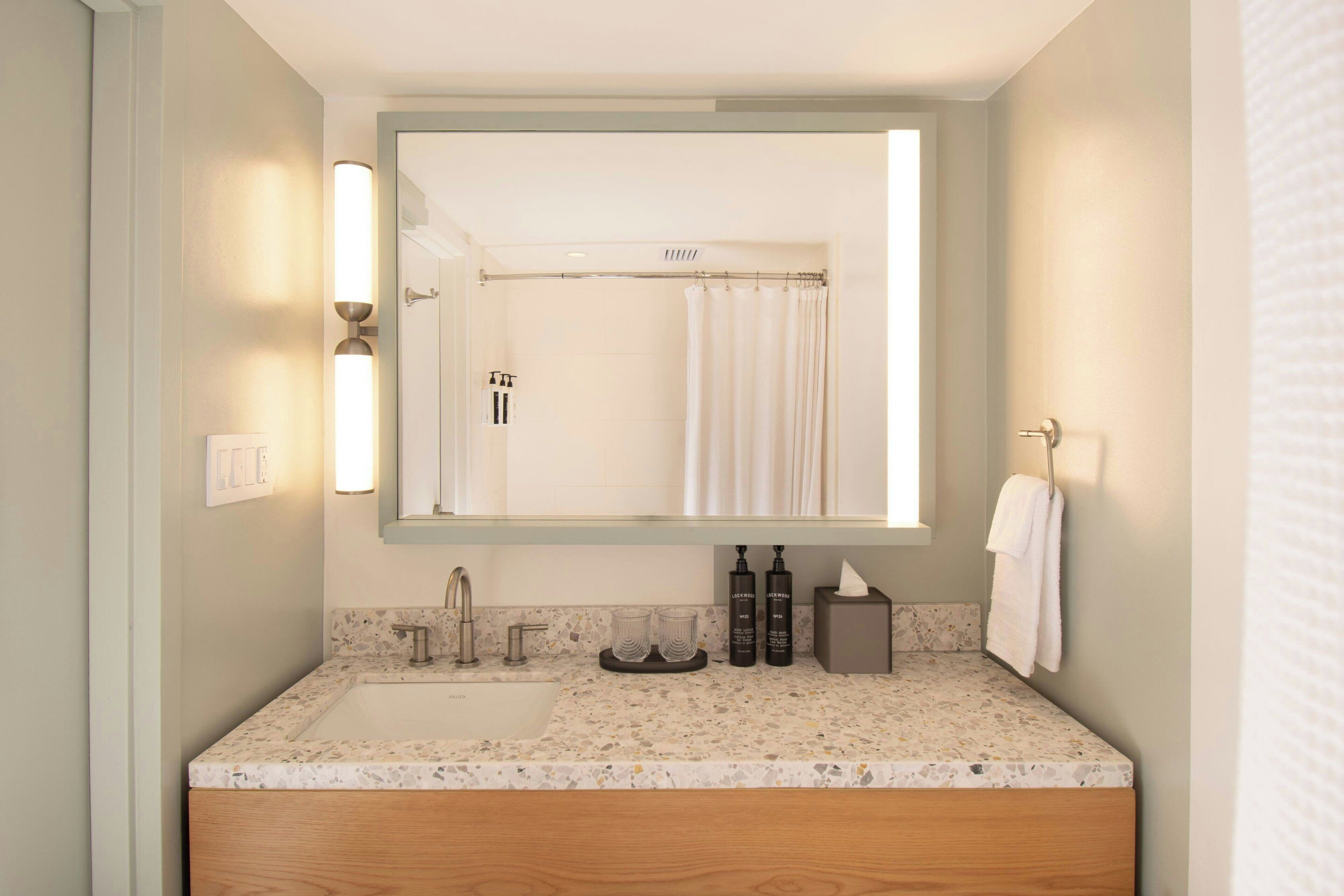 Une salle de bain équipée d’un lavabo, d’un miroir, d’un rideau de douche, d’un porte-serviettes et d’articles de toilette.