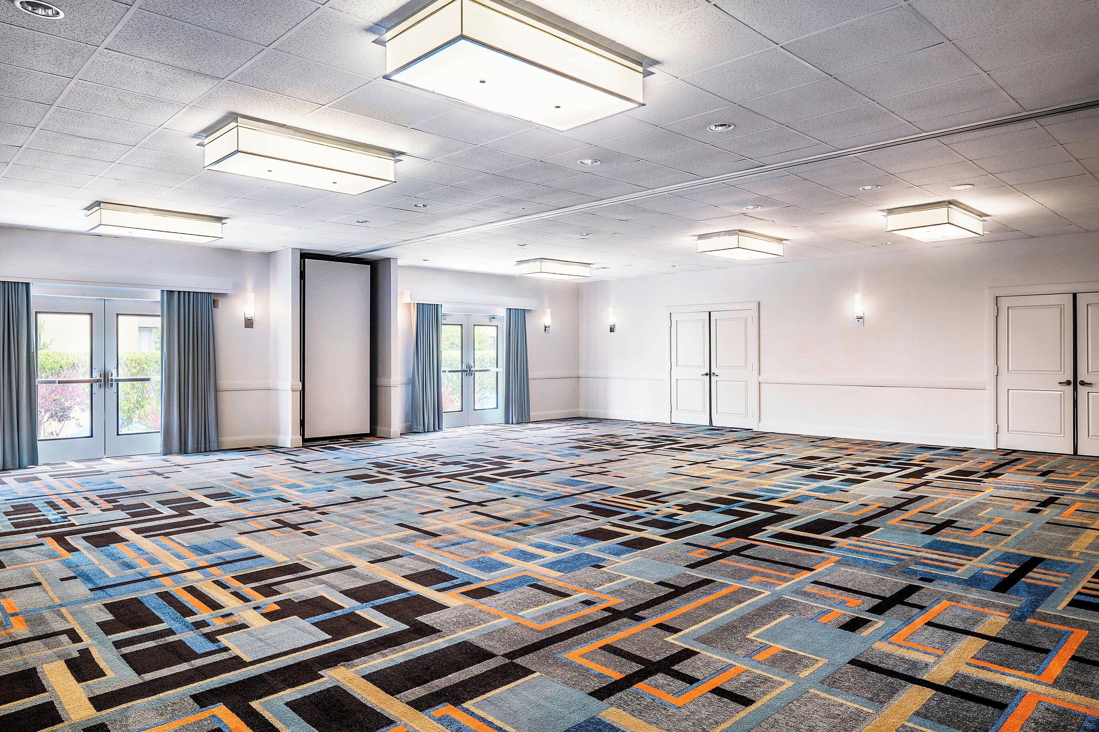A spacious conference room with a patterned carpet, white walls, and multiple doors.