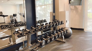 A gym with weightlifting equipment, a mirror, and a TV mounted on the wall. - Marin Hilltop Hotel (San Rafael)