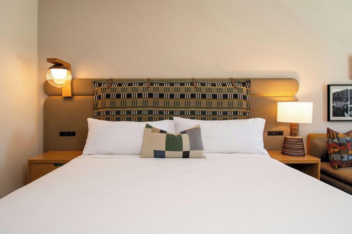 A neatly made bed with a patterned headboard, a bedside lamp, and a framed picture on the wall.