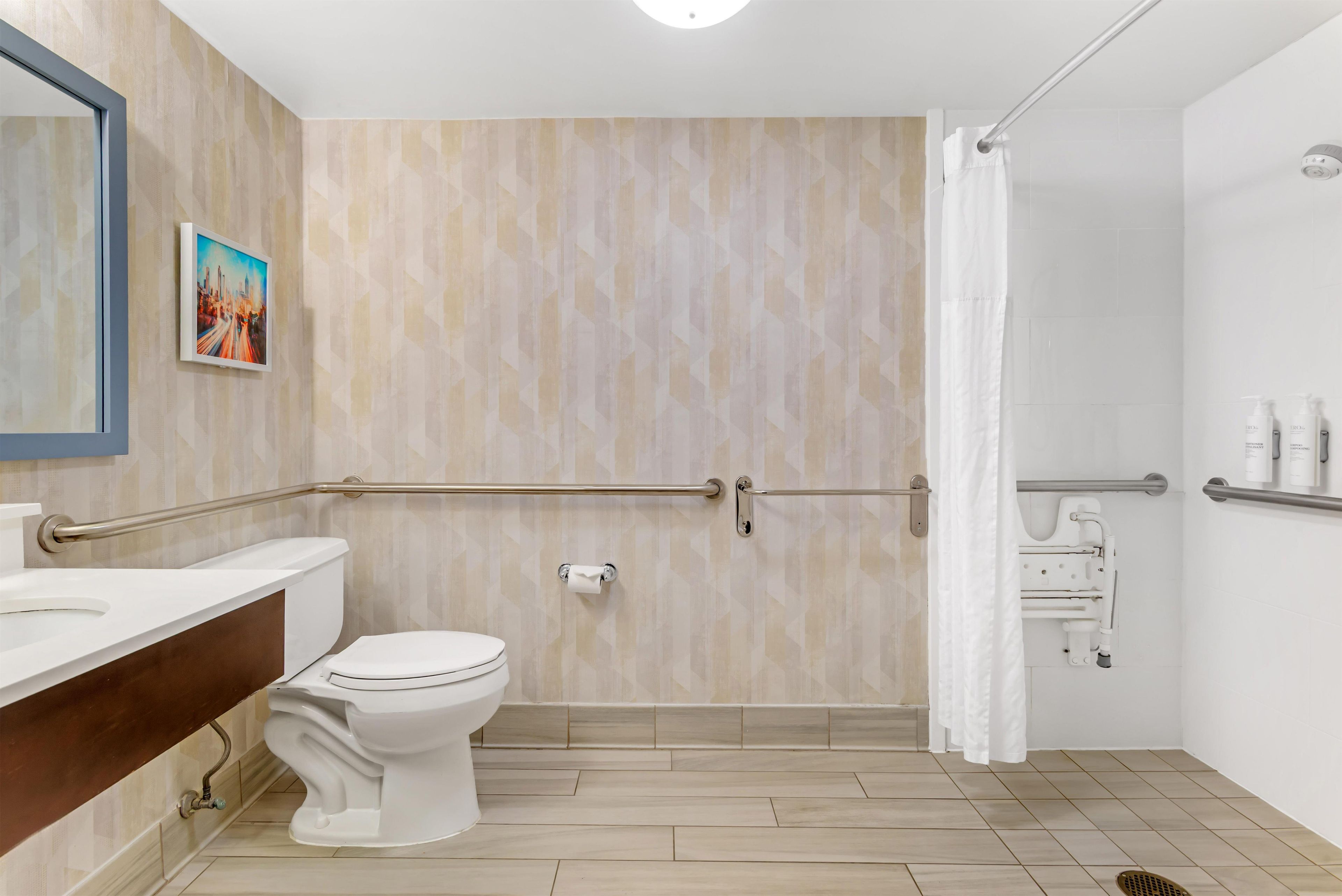 A bathroom with a toilet, a sink, a shower with a grab bar, and a towel rack.