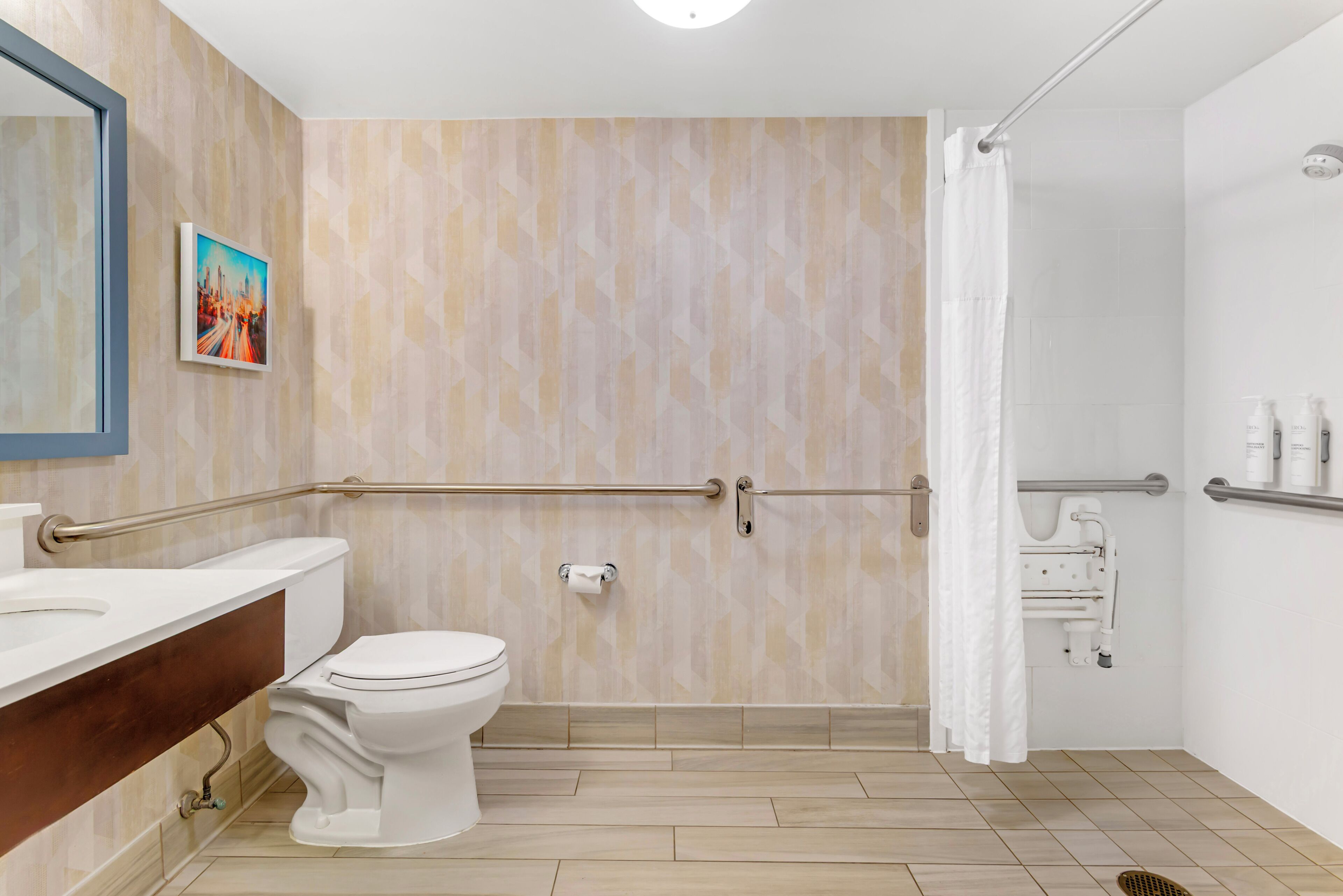 Un baño con inodoro, lavamanos, ducha con barra de apoyo y secamanos.